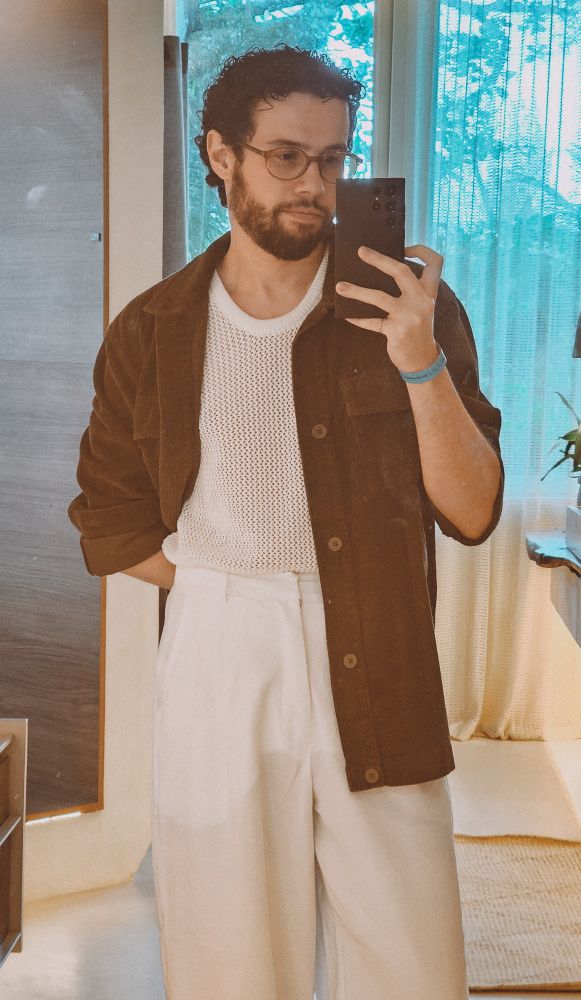 uma selfie no espelho, estou vestindo uma calça branca de cintura alta e uma camiseta de tricô furadinha, com uma camisa de botão escura por cima 