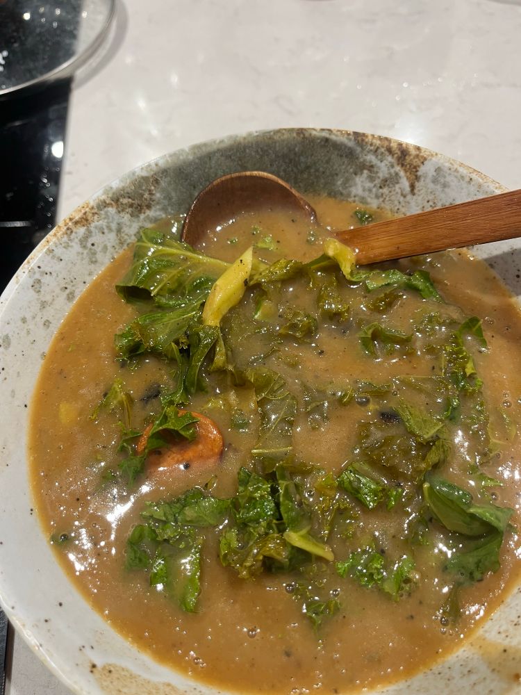 An orange brown soup with kale and chorizo visible in it 