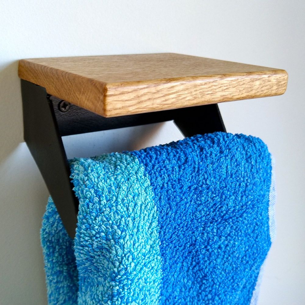 A small black steel hand towel rail with integrated oak shelf. A stripey towel hangs from it.
