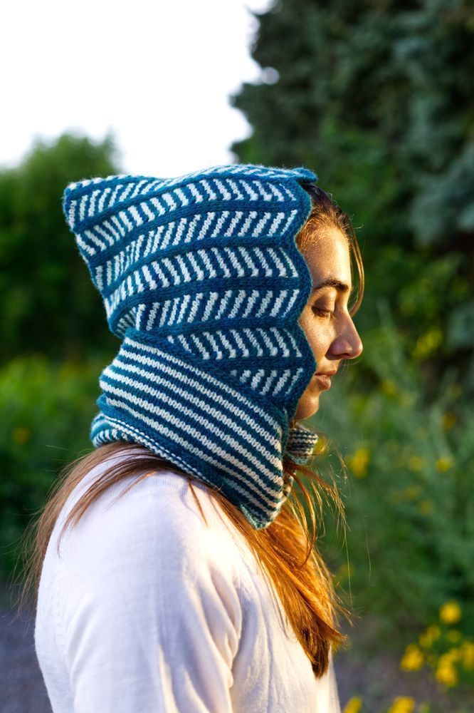 Shena Tschofen in a garden wearing her blue and white Lollyzag Hood made with Norwood yarn in Pirate Cove and Natural Cream