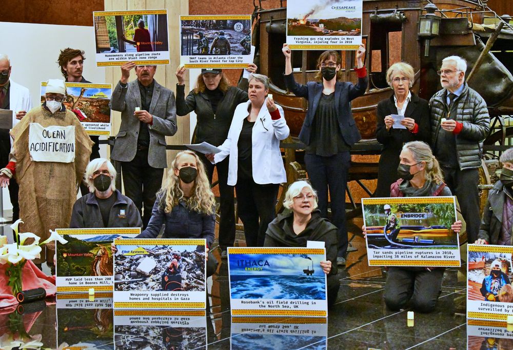 Protesters in front of a stagecoach, holding signs listing many of the environmentally destructive and colonially exploitive projects financed by Wells Fargo.  San Francisco, Feb 2024