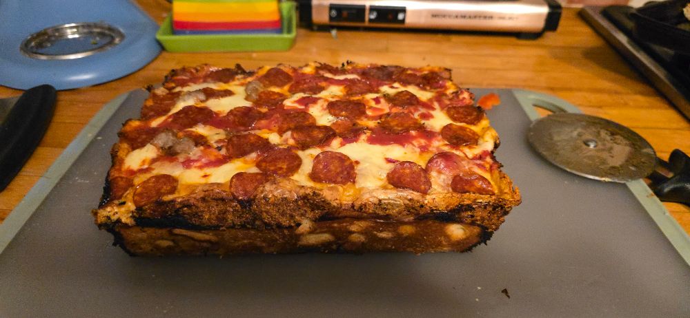 A Detroit style pizza with pepperoni on a cutting board with a pizza cutter next to it.