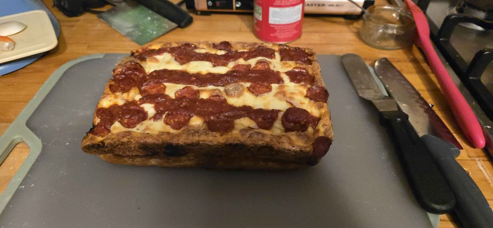 An uncut Detroit style pizza with three rows of sauce and covered in pepperoni and cheese