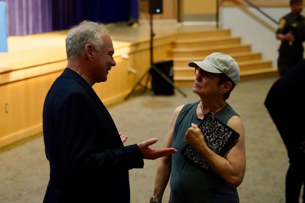 Senator Kaine speaks with a woman in front of a stage. 