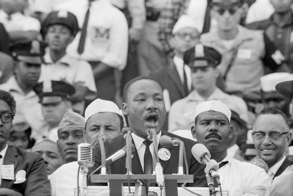 Dr. King stands in front of a podium with multiple microphones, delivering his speech in Washington. 