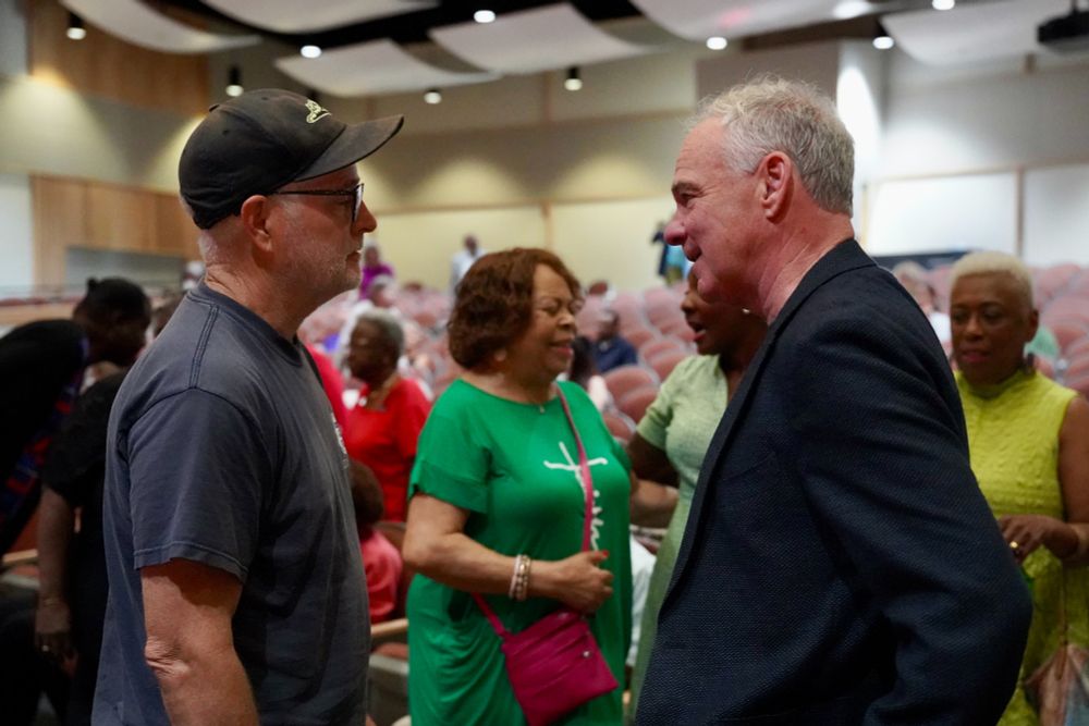Senator Kaine speaks with a man in a crowded room. 