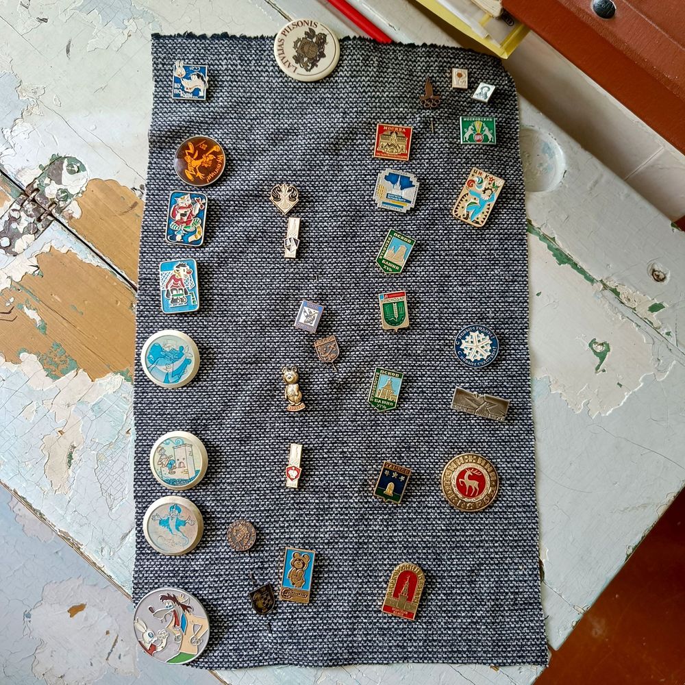 A bunch of pins from the Soviet-era on a chipped old school bench, including Nu-Pogodi and Misha the bear.