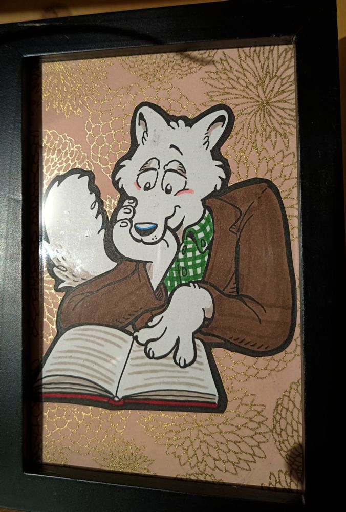 Framed painting of an anthro arctic fox in a brown jacket and plaid green shirt reading a book, pink background with golden flower patterns.