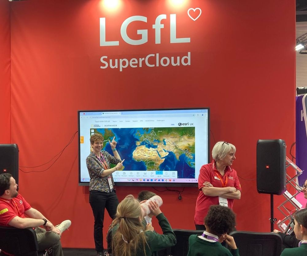 Katie grinning on the lgfl stand pointing at a screen showing Mapmaker 