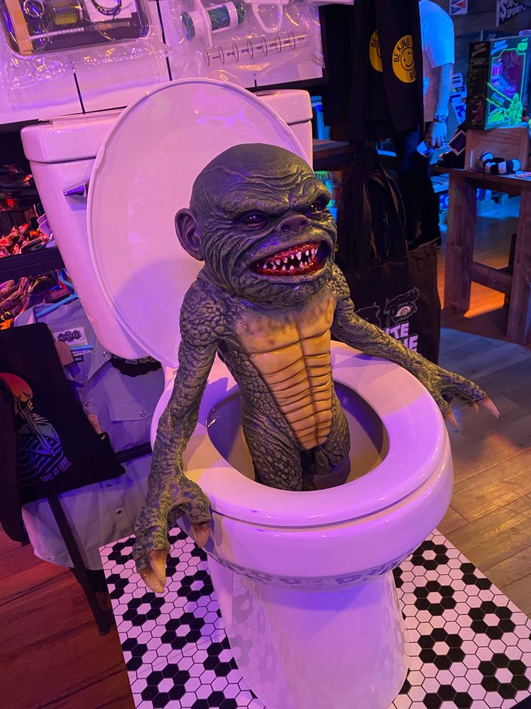 Photo of a plastic creature coming out of a prop toilet made to resemble the cover of the horror move “ghoulies” 