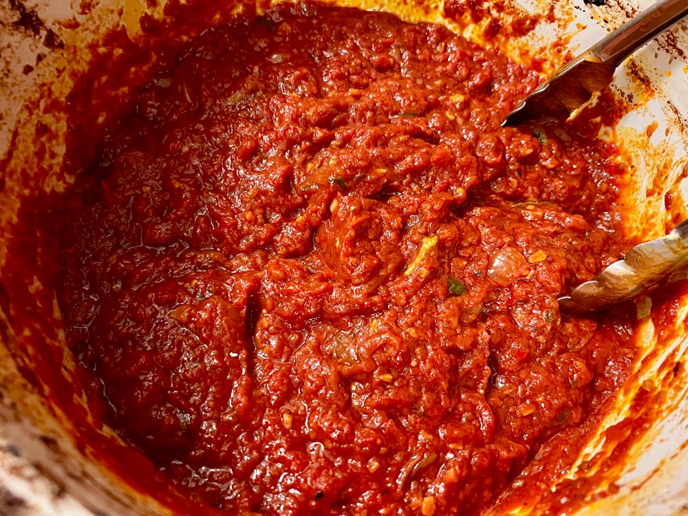 A pot of deep dark red long cooked tomato sauce.