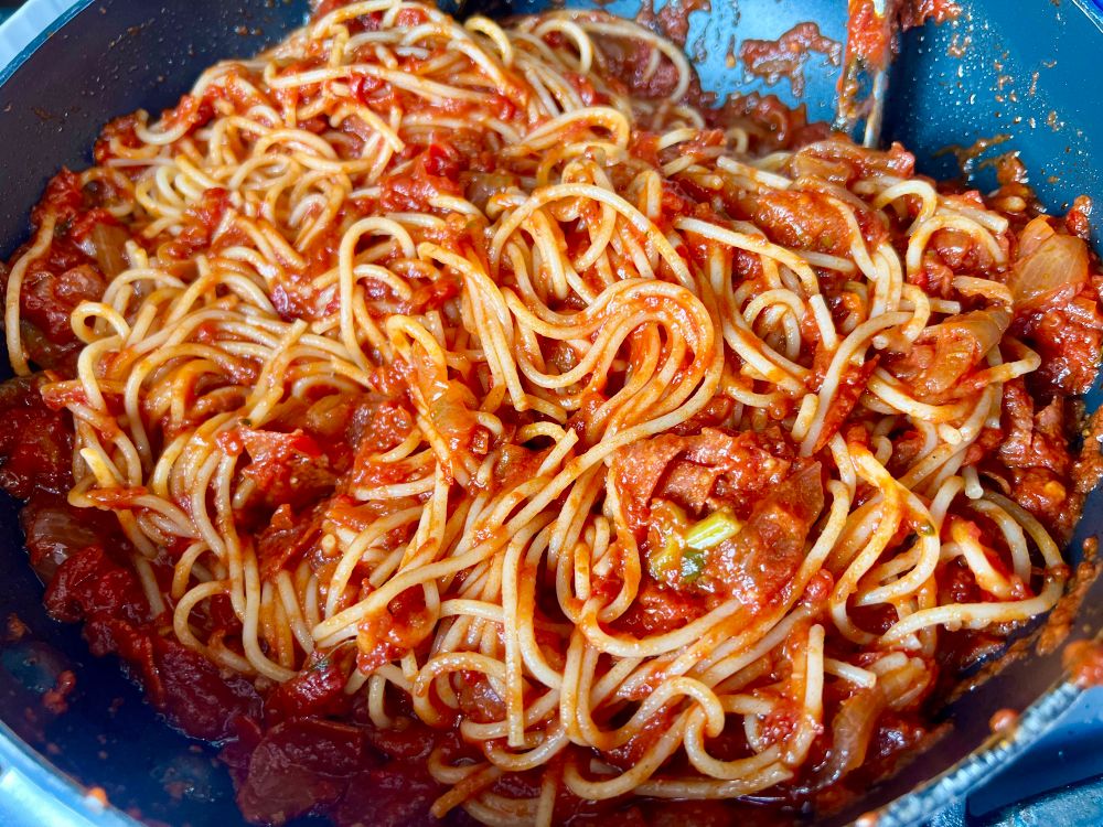Thin spaghetti mixed with chunky tomato sauce in the pot.