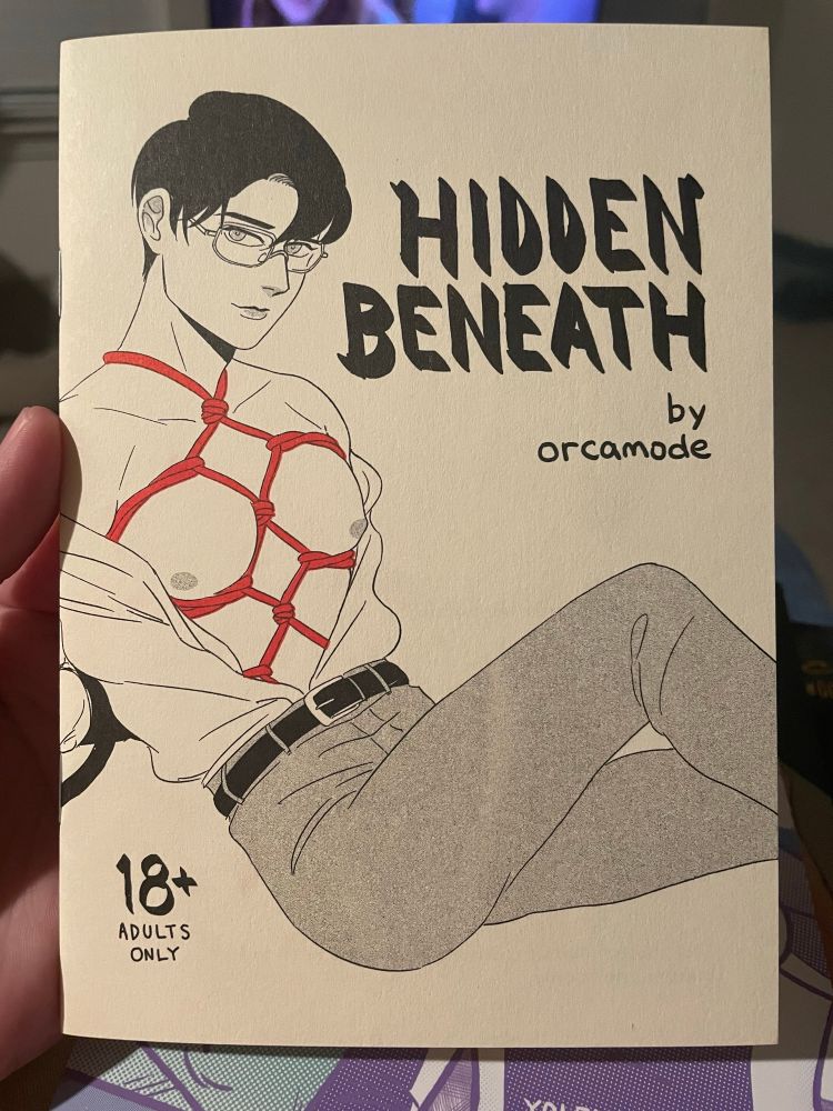 18+ comic book called Hidden Beneath by Orcamode. The cover is black and white if a business man with his shirt open revealing red ropes tied across his chest