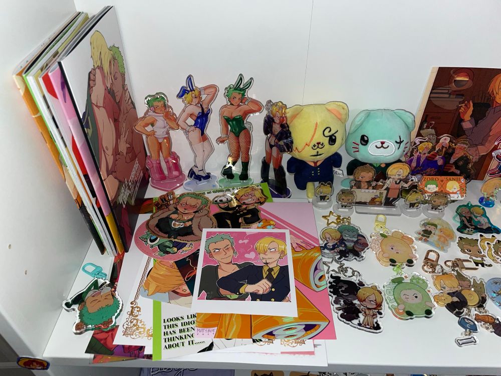 Closer view of my Zosan/Sanzo shelf, standees, art books, Neko plushes, stack of art prints and stickers, and lots of keychains