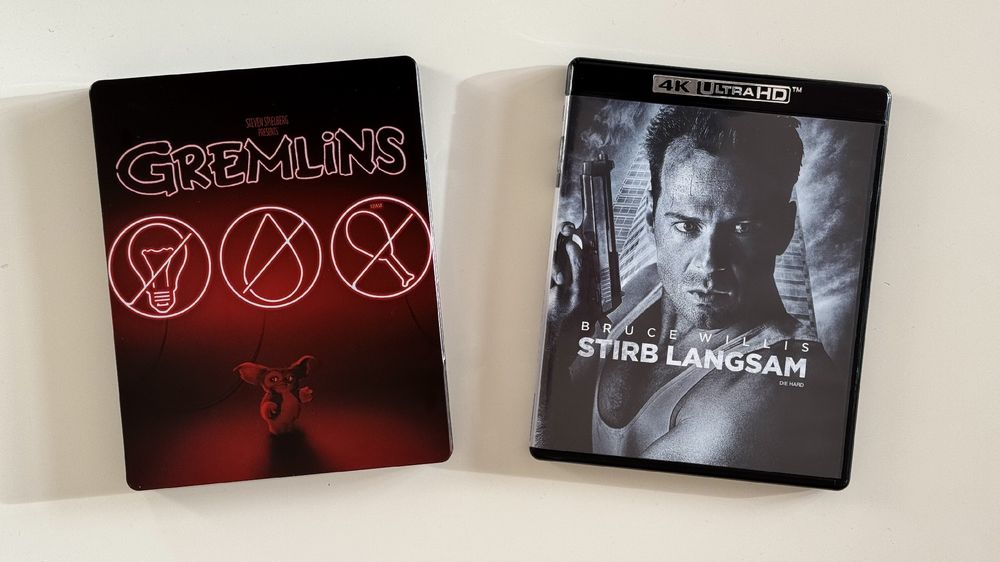 The image features two movie cases: on the left, a steelbook edition of "Gremlins" with neon graphics and a character illustration; on the right, a 4K Ultra HD edition of "Die Hard," showcasing Bruce Willis.
