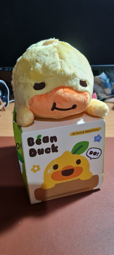 A yellow duck with orange bill posture corrector plushie, still in packaging. 