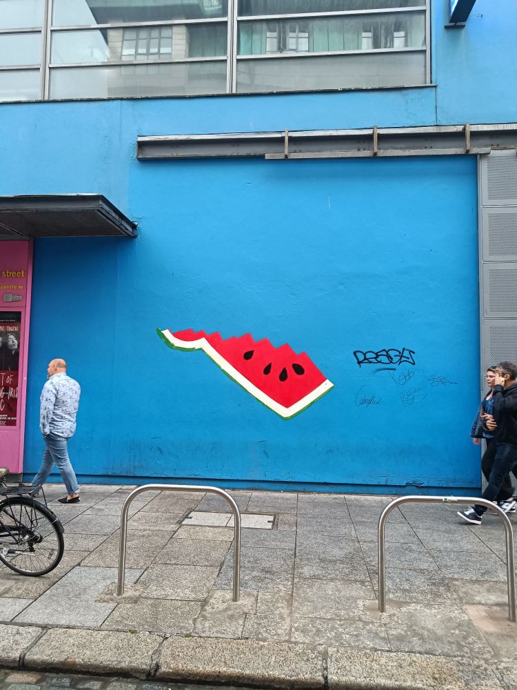 Section of a watermelon for Palestinian solidarity on a blue wall. A reference to a Repeal the 8th mural removed from the project arts centre in 2018.