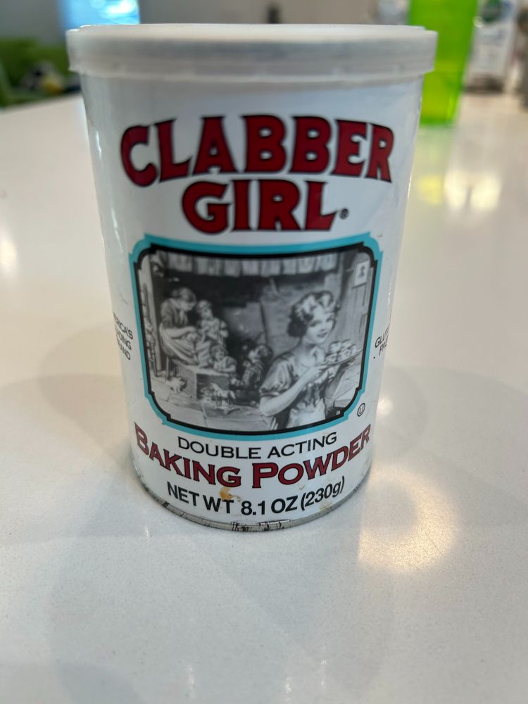 A tin of Clabber Girl brand baking powder sits on a counter