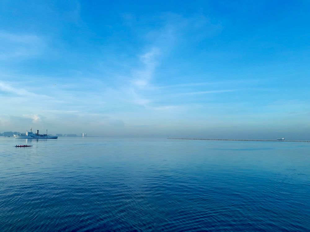 Manila Bay early morning in 2018. There is a ship and dragonboat team in front of the Manila skyline.