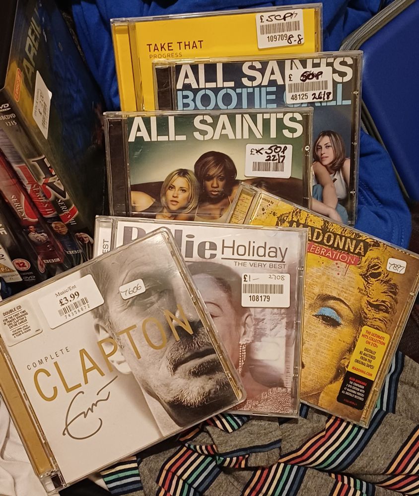 A stack of six CDs: Progress by Take That, All Saints and Bootie Call by All Saints, Complete Eric Clapton, The Very Best of Billie Holiday and Celebration by Madonna.