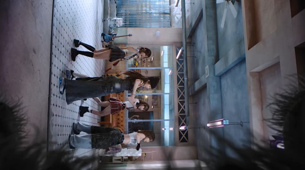 Captura de tela de um momento do clipe em que o ângulo da câmera está virado 90º graus, como se a aranha estivesse olhando as artistas dançando diretamente da parede.