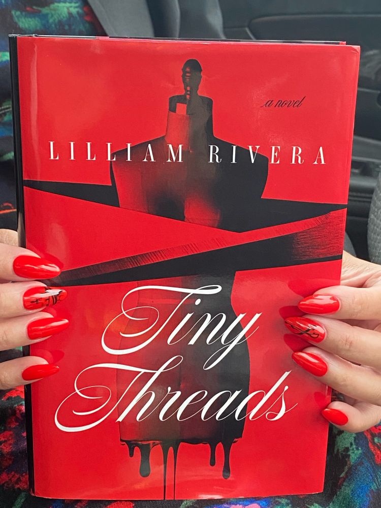 Photo of the book Tiny Threads being held up with someone with long red nails.