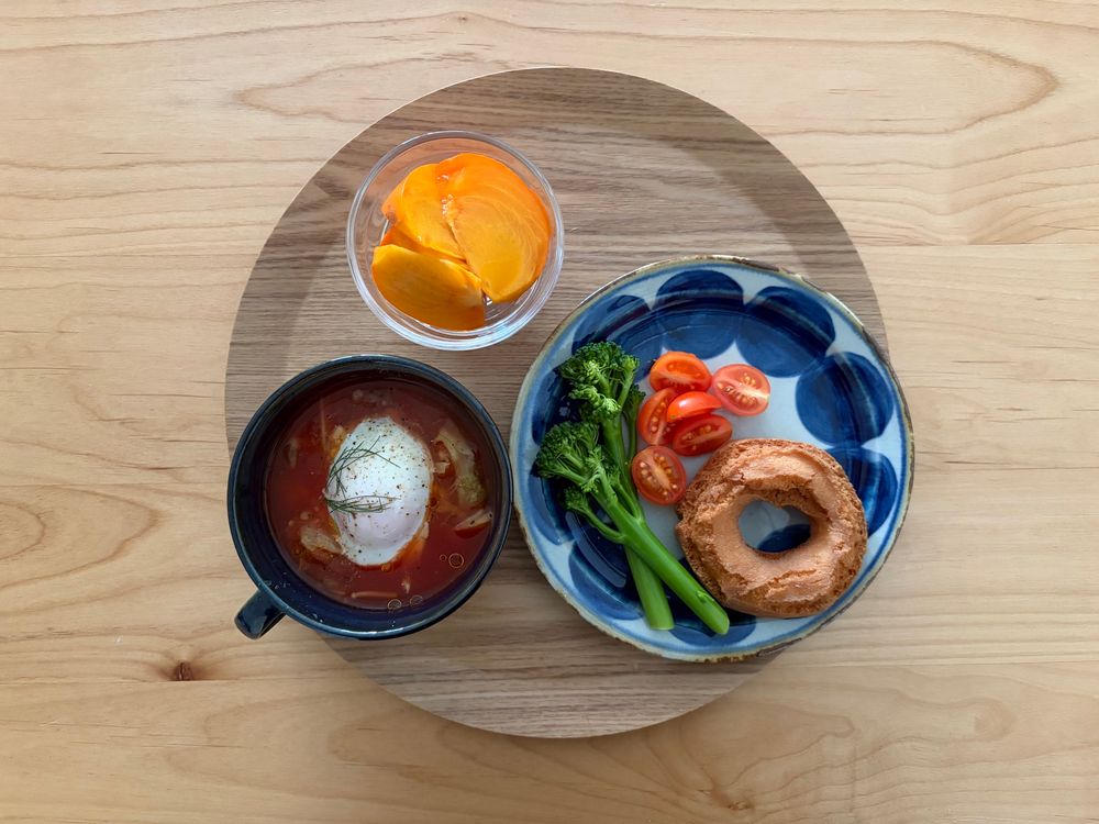 スープカップにキャベツときのこのトマトスープ温玉入り、お皿に茎ブロッコリーとミニトマトとドーナツ、ガラス豆鉢に柿