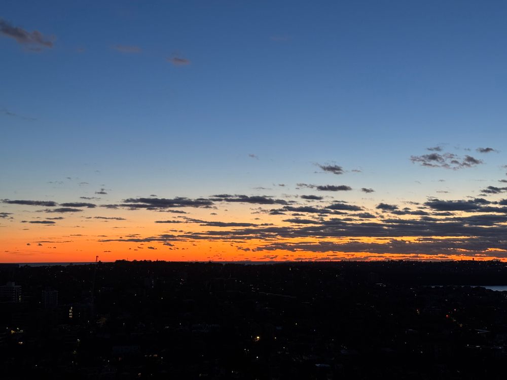 Dark blue and orange sky with dark clouds above the horizon over an urban landscape.