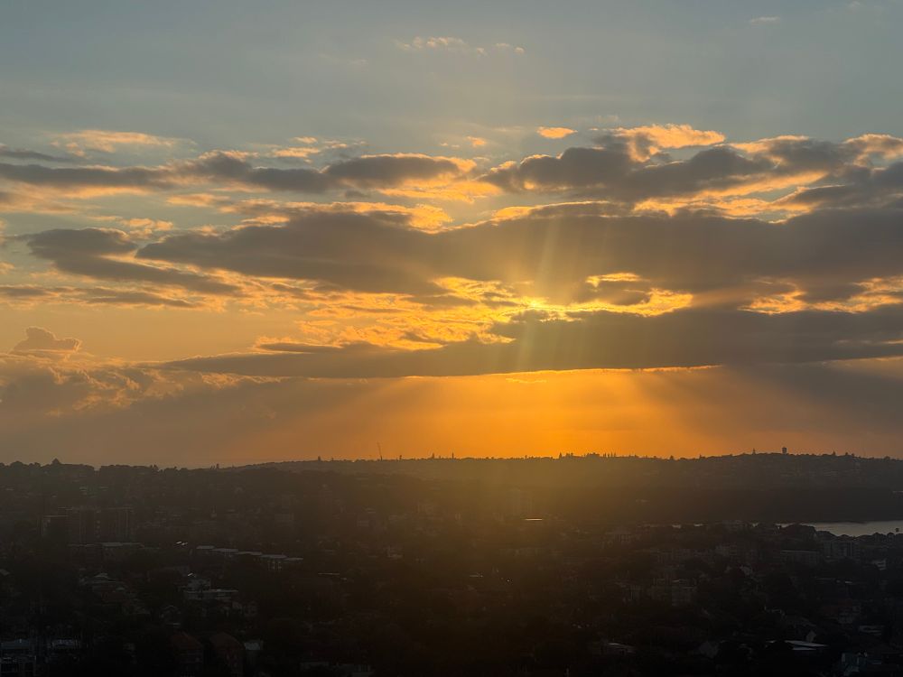 The golden sun peeks through dark grey cloud cover over an urban landscape 
