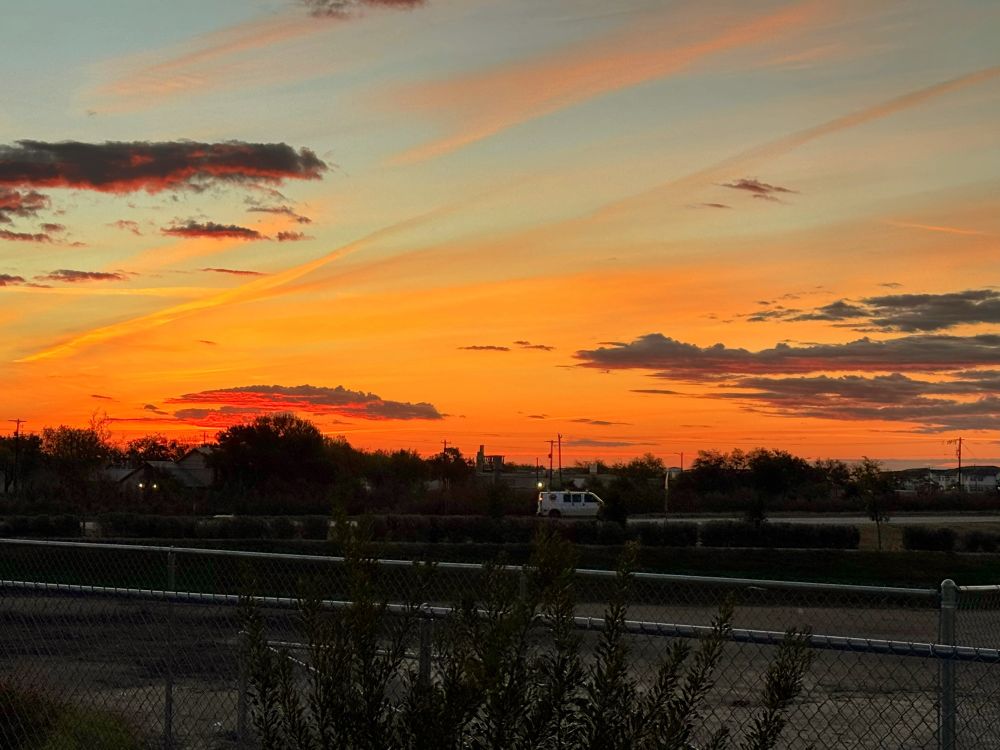 Orange sunrise poking through thin clouds over an interstate