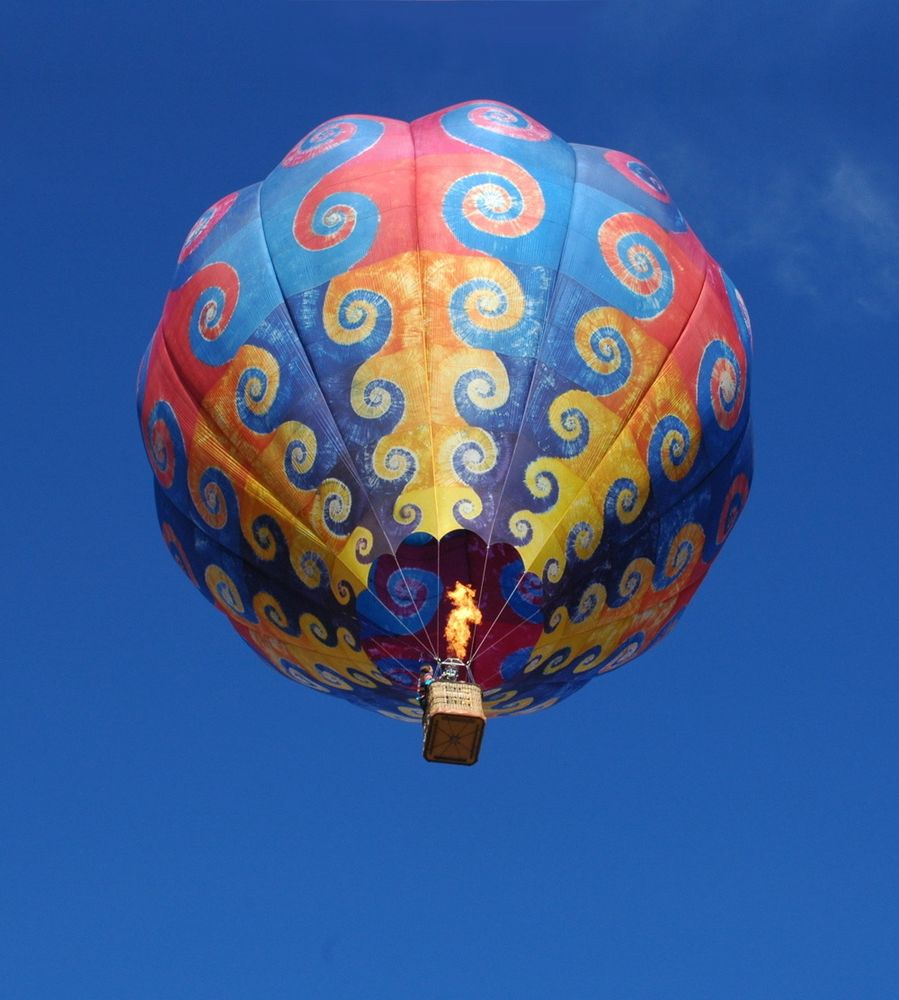 Gloria Caeli, a tiedyed balloon against a blue sky background.