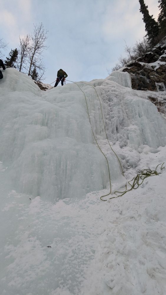 An ice climber begins the rappel off of the top of an ice wall.