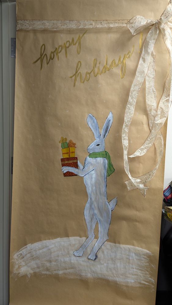 Decorated office door with large ribbon and painting of a snowshoe hare carrying presents.