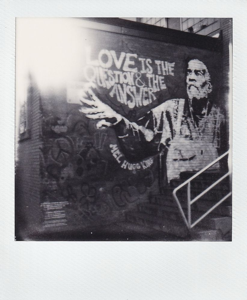 Follow the Light: B&W Polaroid SX-70 film photo with light leak and sunlight white out of mural honoring legendary Boston community organizer and activist Mel King with quote: "Love is the Question and the Answer." Shot with a Polaroid SX-70 camera for Polaroid Week on Flickr. South End Boston.