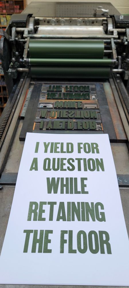A letterpress printed poster in green ink, reading I YIELD FOR A QUESTION WHILE RETAINING THE FLOOR