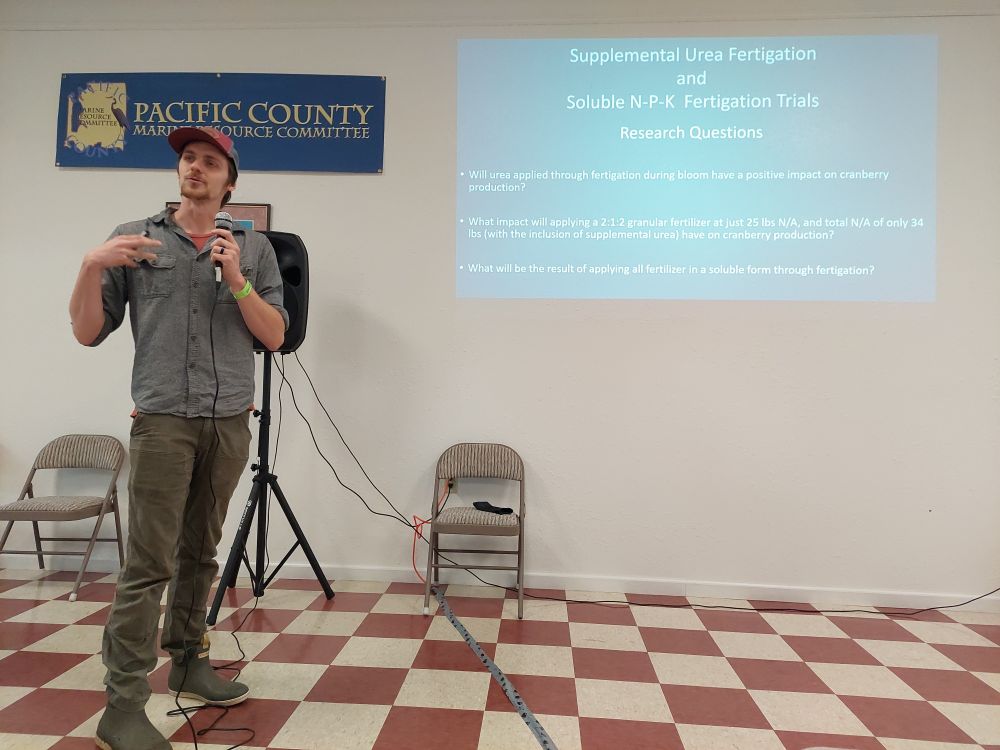 Alex Gregory, OceanSpray AgScientist, giving a talk on fertilizer treatments. He talks into a mic in front of a PowerPoint slide showing fertilizer treatment information.
