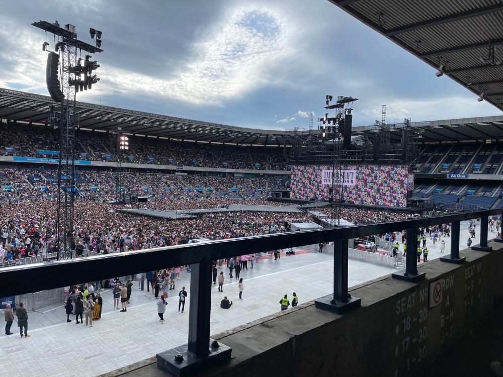 A photo of Murrayfield stadium in Edinburgh.  There is a screen saying Taylor Swift eras tour and lots of people standing around in front of the stage
