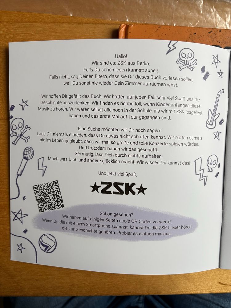 Text im Inneren des Kinderbuchs: „Hallo!
Wir sind es: ZSK aus Berlin.
Falls Du schon lesen kannst: super!
Falls nicht, sag Deinen Eltern, dass sie Dir dieses Buch vorlesen sollen, weil Du sonst nie wieder Dein Zimmer aufräumen wirst.
Wir hoffen Dir gefällt das Buch. Wir hatten auf jeden Fall sehr viel Spaß, uns die Geschichte auszudenken. Wir finden es richtig toll, wenn Kinder anfangen, diese Musik zu hören. Wir waren selbst alle noch in der Schule, als wir mit ZSK losgelegt haben und das erste Mal auf Tour gegangen sind.
Eine Sache möchten wir Dir noch sagen:
Lass Dir niemals einreden, dass Du etwas nicht schaffen kannst. Wir hätten damals nie im Leben geglaubt, dass wir mal so große und tolle Konzerte spielen würden.
Und trotzdem haben wir das geschafft.
Sei mutig, lass Dich durch nichts aufhalten.
Mach was Dich und andere glücklich macht. Wir wissen, Du kannst das!
Und jetzt viel Spaß,
*ZSK*
Schon gesehen?
Wir haben auf einigen Seiten coole QR Codes versteckt.
Wenn Du die mit einem Smartphone scannst, kannst Du die ZSK-Lieder hören, die zur Geschichte gehören. Probier es einfach mal aus.