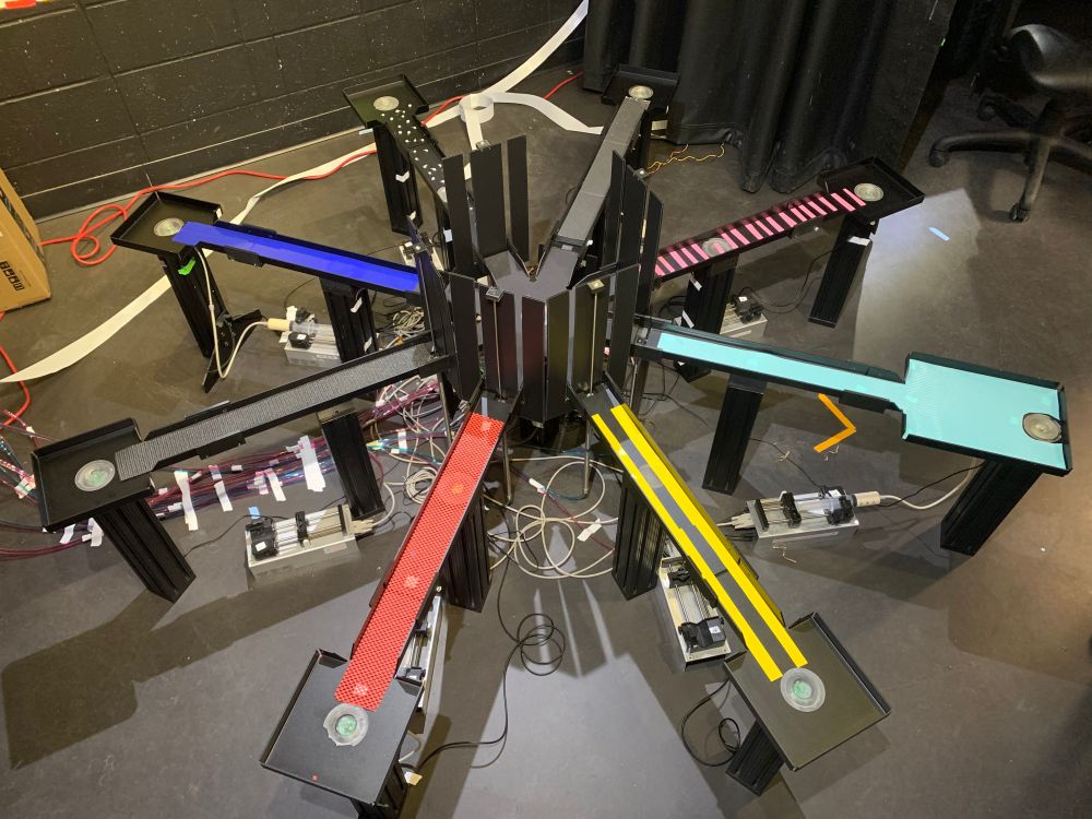 An 8-arm radial maze is depicted. Each of the 8 arms is covered in a different context that varies in color and texture. In the center of the maze, 8 barriers are present that control access to the 8 arms. At the end of each arm is a reward well where rats can receive a liquid reward.
