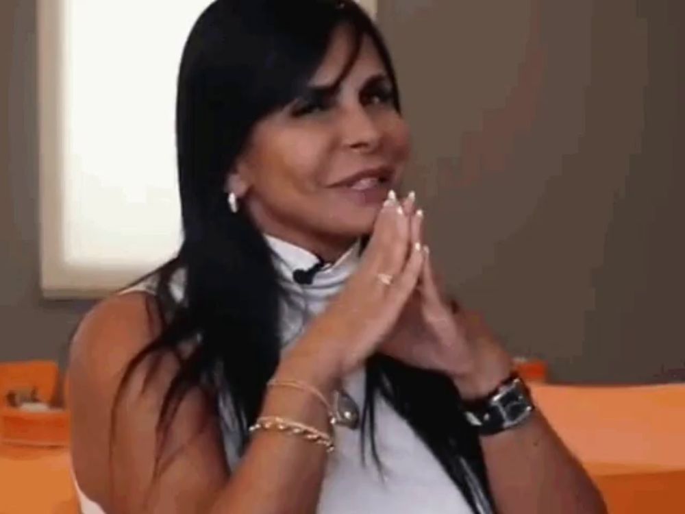 a woman with long black hair is sitting at a table with her hands folded .