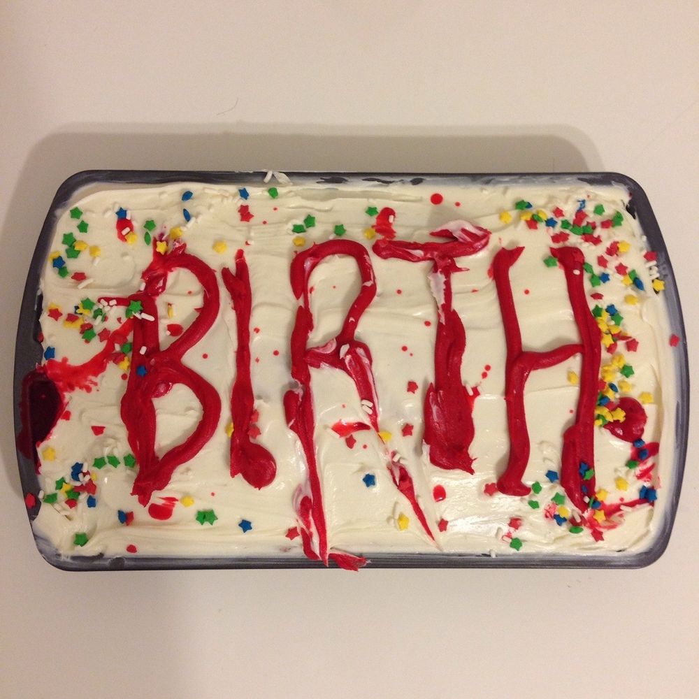 A cake with white frosting in a pan. On top, in red frosting, the word "BIRTH" has been spelled out in jagged letters. It's covered with multi-colored star shaped sprinkles.