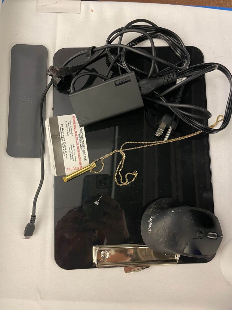 A black clipboard, a logitech mouse, a wrist rest, a stud earring, a whistle necklace, and a computer power cord, and a parking card. 