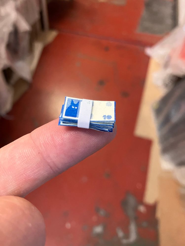 A miniature stack of cat banknotes wrapped in a paper band balancing on the end of my finger.