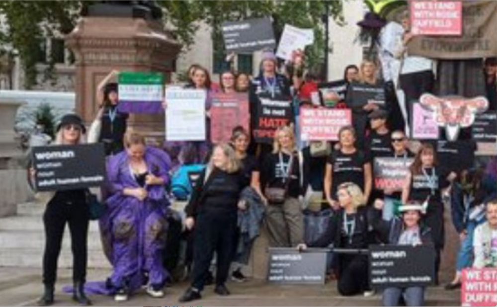 Close-up on the left half of the Bad Medical Taker's Xitter banner picture showing an anti-trans demonstration, people holding various signs including those of a purported dictionary definition of “woman”