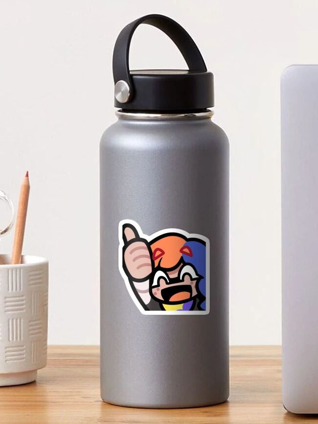 A silver reusable water bottle with a black carrying handle is shown on a wooden surface. The bottle features a colorful sticker of an animated character with orange hair and blue hair with a gray outfit, giving a thumbs-up and smiling enthusiastically. To the left, there is a white cup holding a pencil, and to the right, part of a gray laptop is visible.
