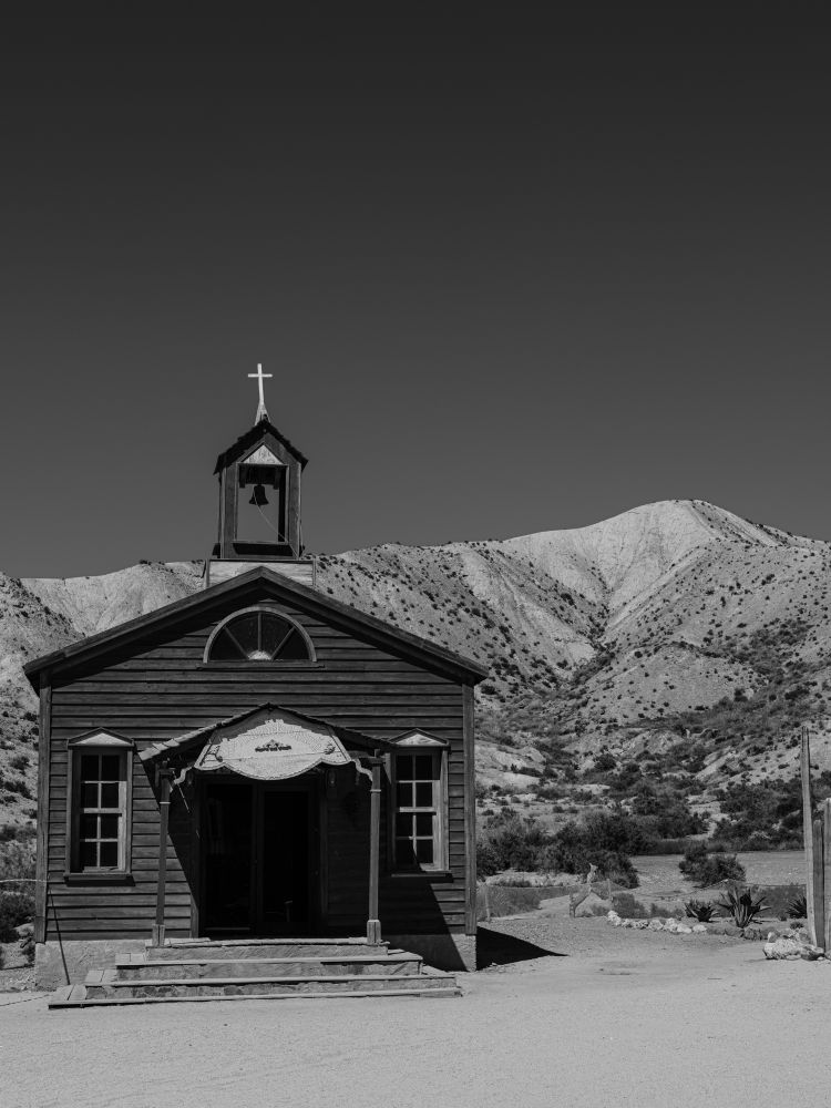 A small church in black and white stands in front of a tall mountain. Photo was taken in Almeria on a former western film set.