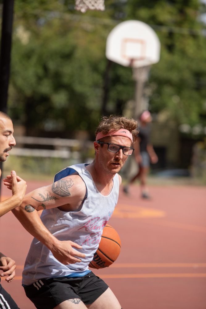 player wearing a headband and glasses dribbling a basketball while another person guards him