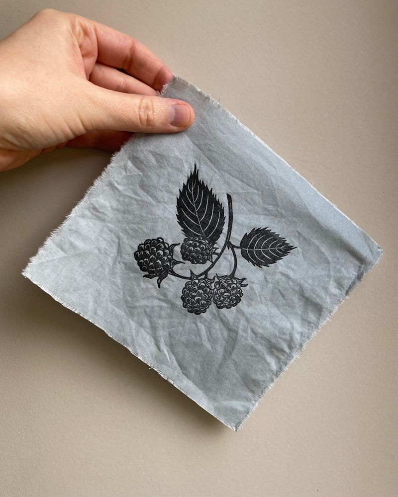 A square of blue grey fabric with a lino printed sprig of blackberries