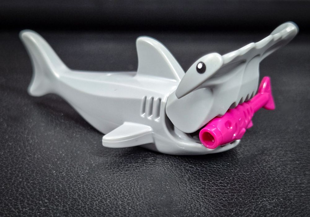 Lego hammerhead shark with magenta Lego fish in its mouth.