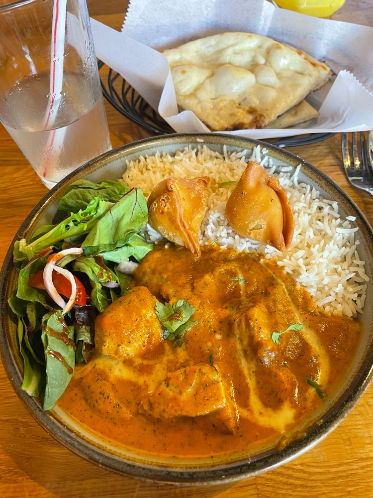 Chicken tikka masala. The curry is an inviting, savory orange-ish color with various specks of spices. Dividing the dish into three portions is salad (spinach as the greens?) with sliced onion and baby tomatoes, drizzled with a dark brown dressing (perhaps a vinaigrette) and basmati rice which has two golf ball sized samosas sitting atop the rice bed. 